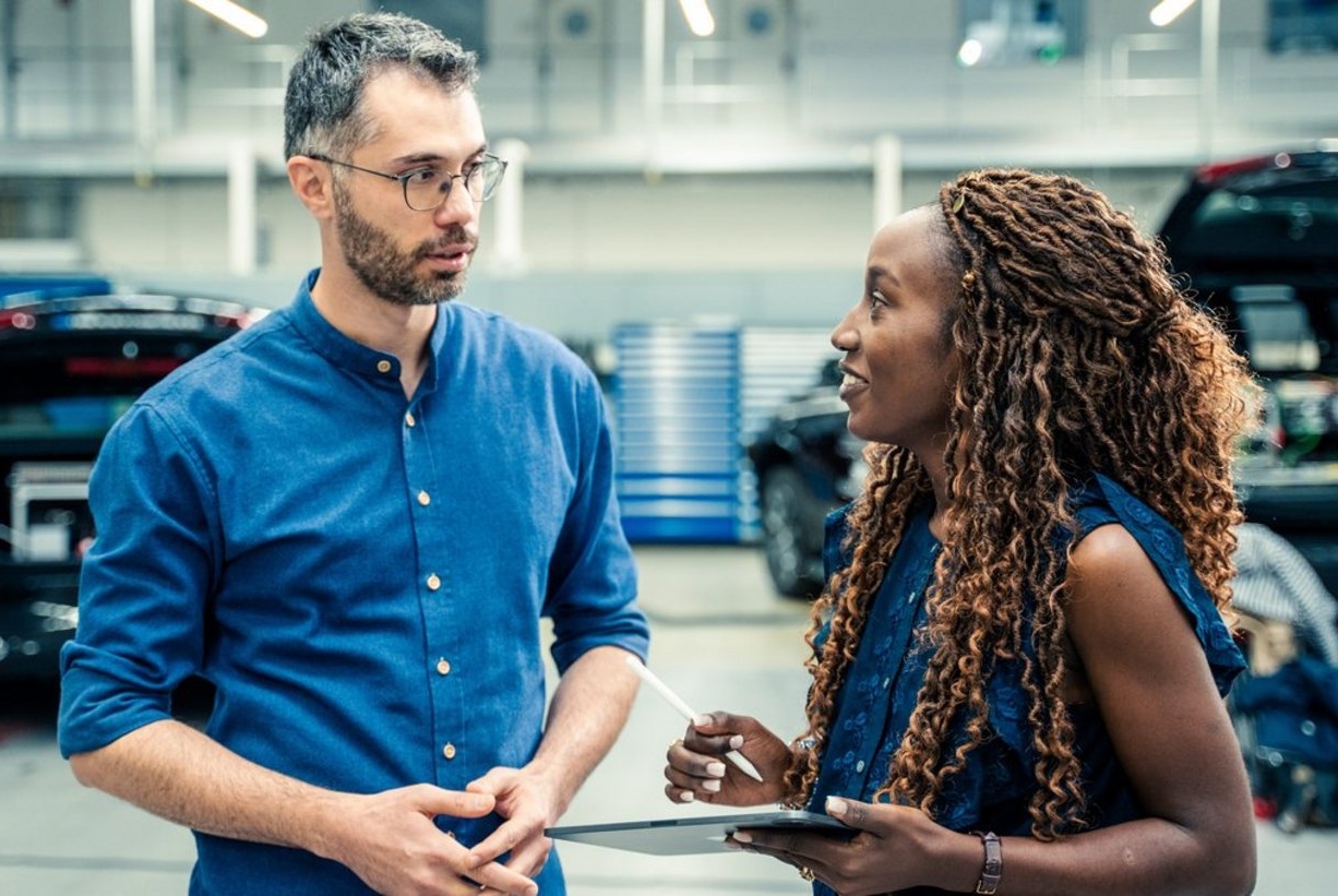 A man and a woman stand in a production hall and look at each other