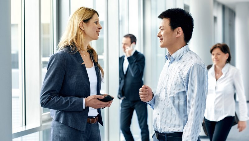 Two men and two women in business outfits walk down a hallway smiling