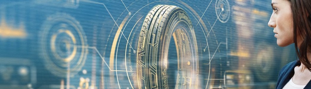 A woman looks at a transparent digital display showing a large, futuristic tire with technical diagrams and data overlays.