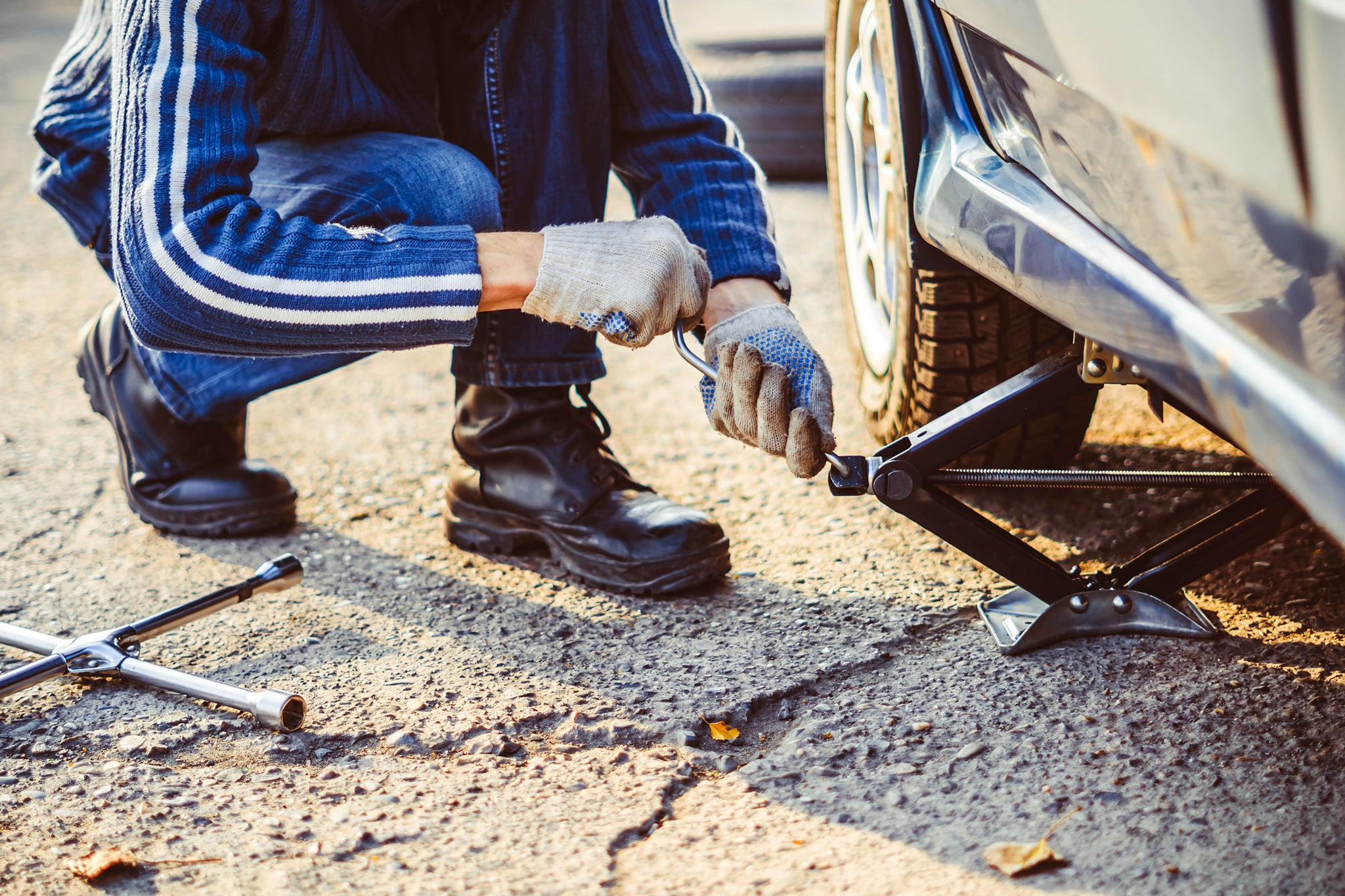 Jacking up a car to change a tyre after a roadside puncture with the hydraulic jack inserted under the bodywork raising the vehicle and the spare wheel balanced on the side.