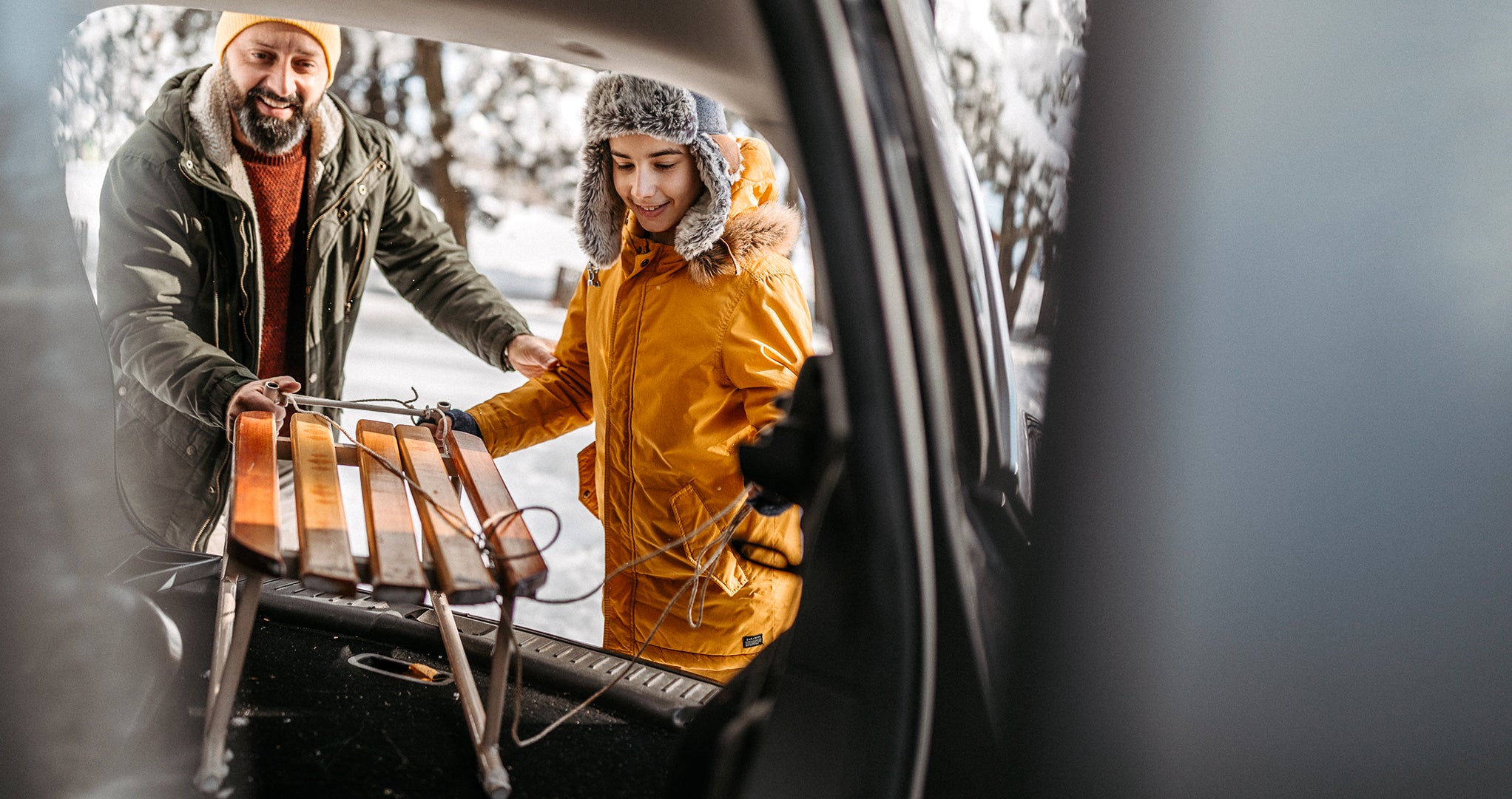 Father and son packing a sled for sledding in the car trunk, dressed in warm clothes.