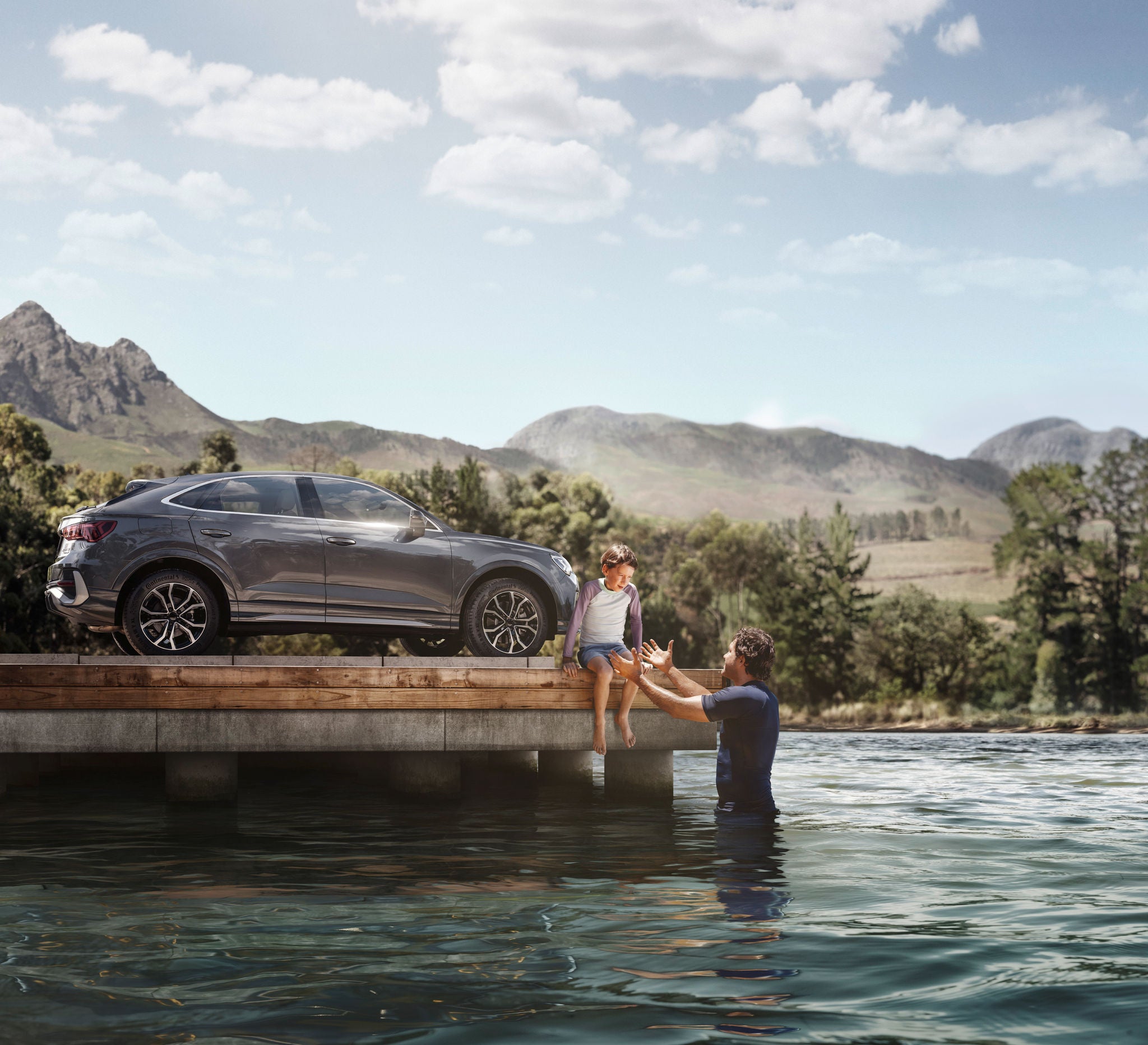 Ein Kind sitzt auf einem Steg, während der Vater im Wassers steht und die Hände zu dem Kind als Hilfestellung ausstreckt. Im Hintergrund steht ein Auto auf dem Steg mit Continental Reifen.