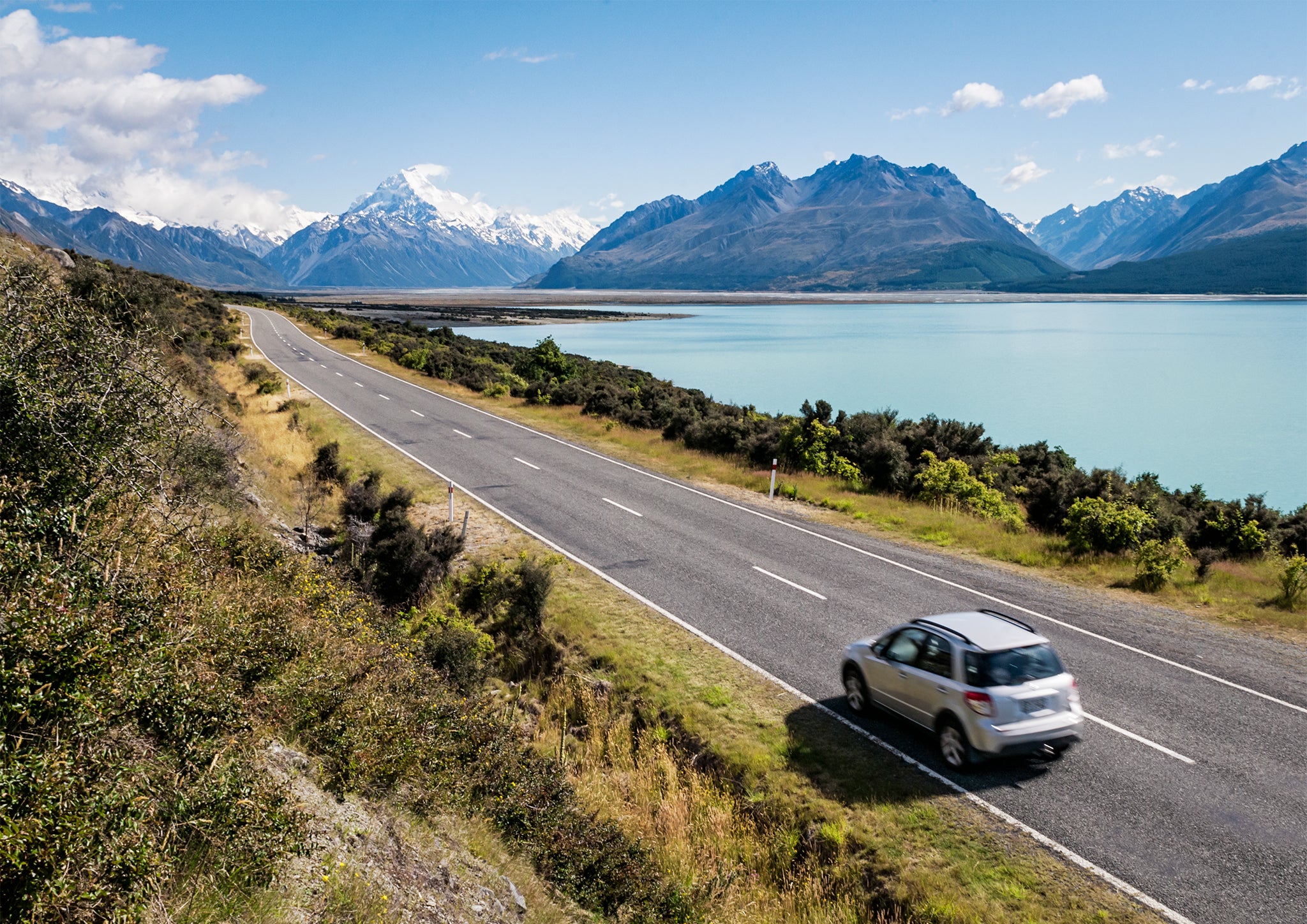 A car on a summer journey next to a lake with mountains in the background.