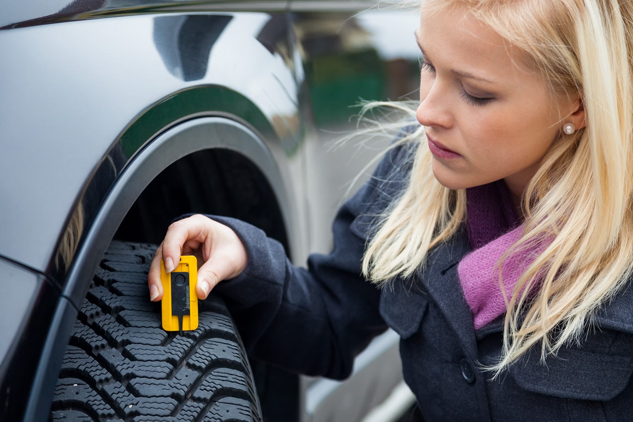 젊은 한 여성이 자동차 타이어의 트레드 깊이를 재고 있습니다.