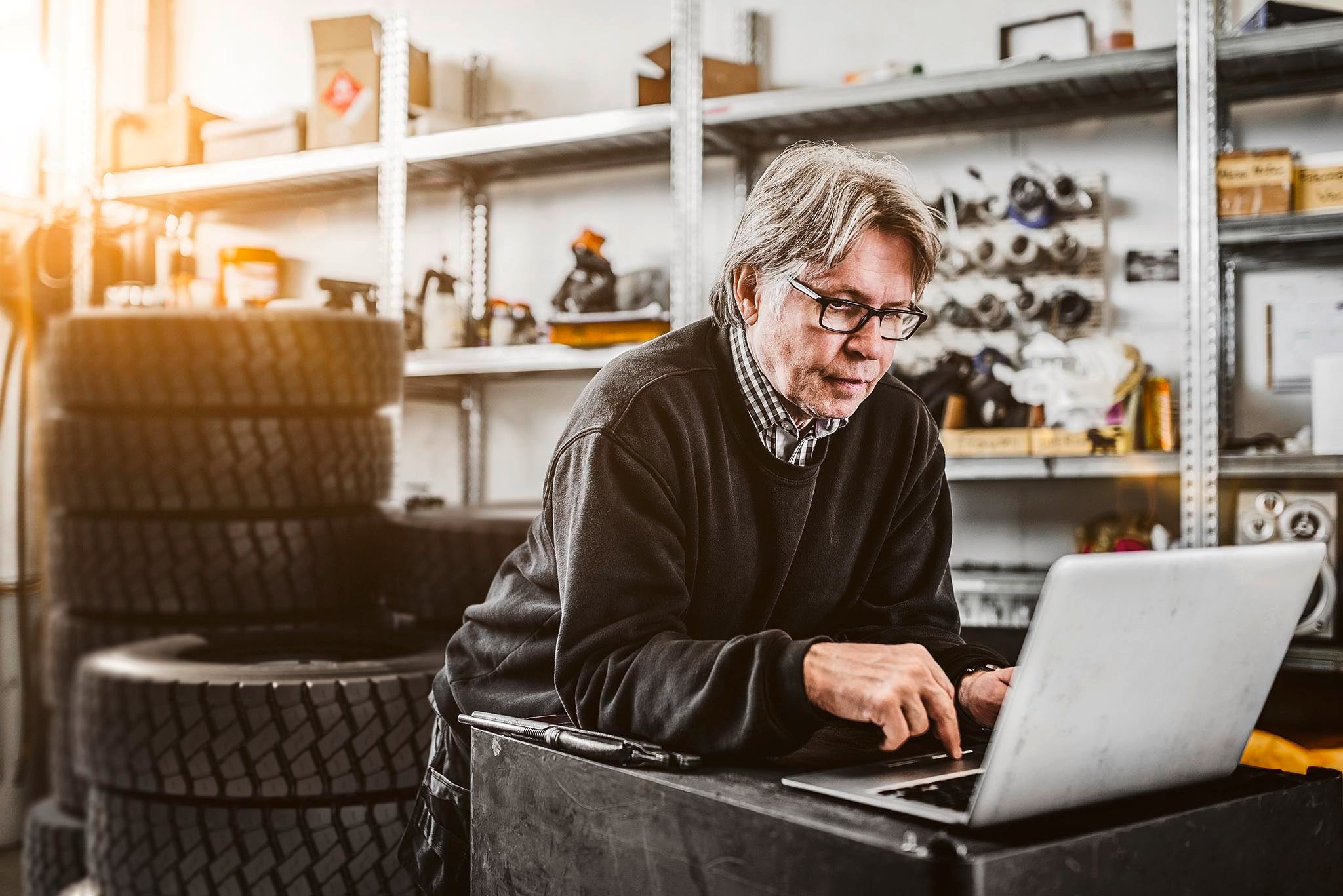 Mécanicien utilisant un ordinateur portable sur des étagères dans un magasin de pneus