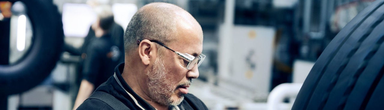 Older man with three-day beard in dungarees checks a tire