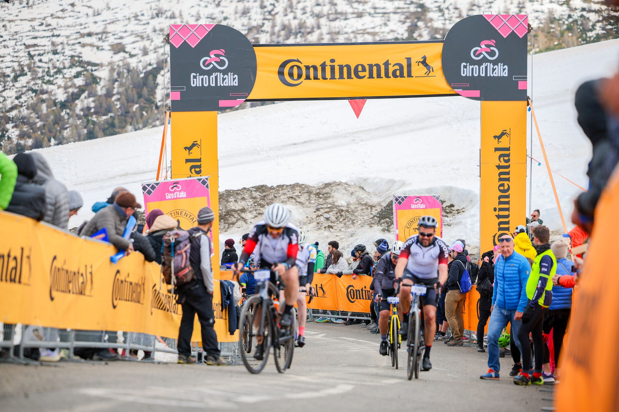 107.º Giro de Italia 2024 - Etapa 15 (imagen de ciclistas durante la prueba del Giro de Italia, con pancartas con la locomotora a lo largo del recorrido y entorno nevado al fondo)