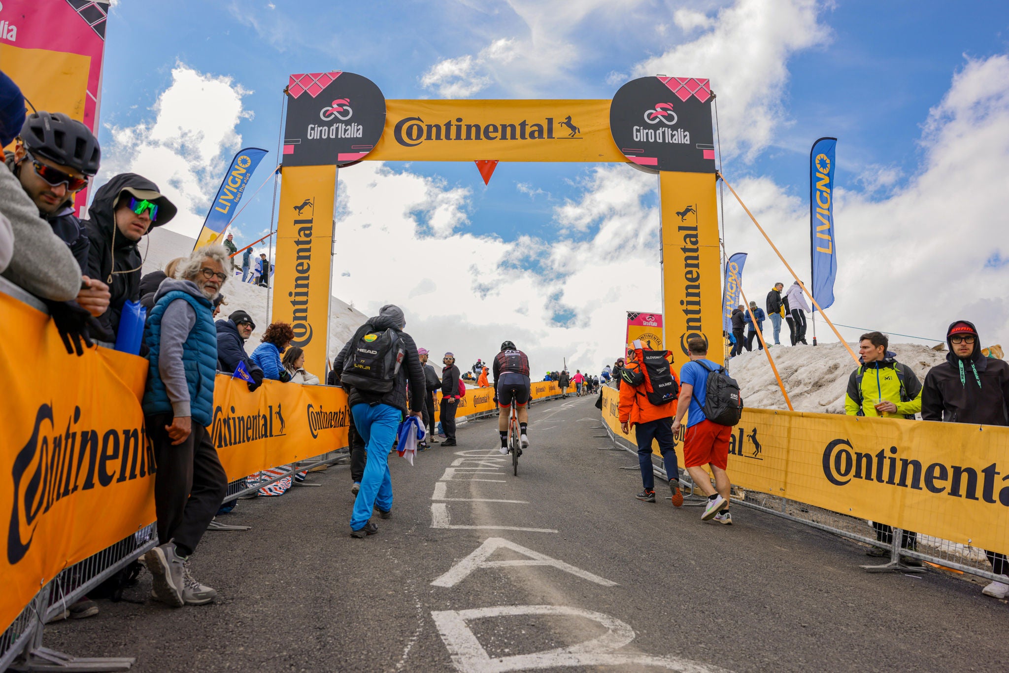 (imagen de ciclistas y aficionados durante la prueba del Giro de Italia, pancartas con el logo de Continental a lo largo del recorrido, entorno invernal, nubes en el cielo al fondo)