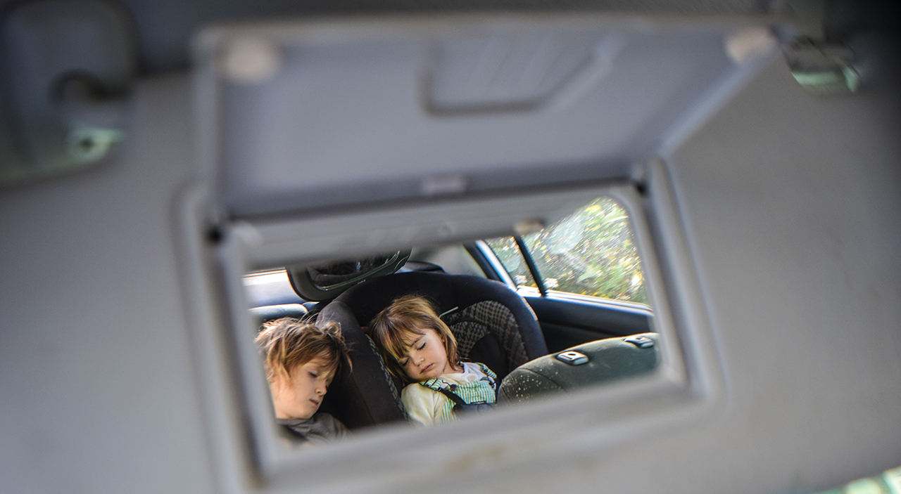 Two little children asleep in the car as seen from the rear vanity mirror