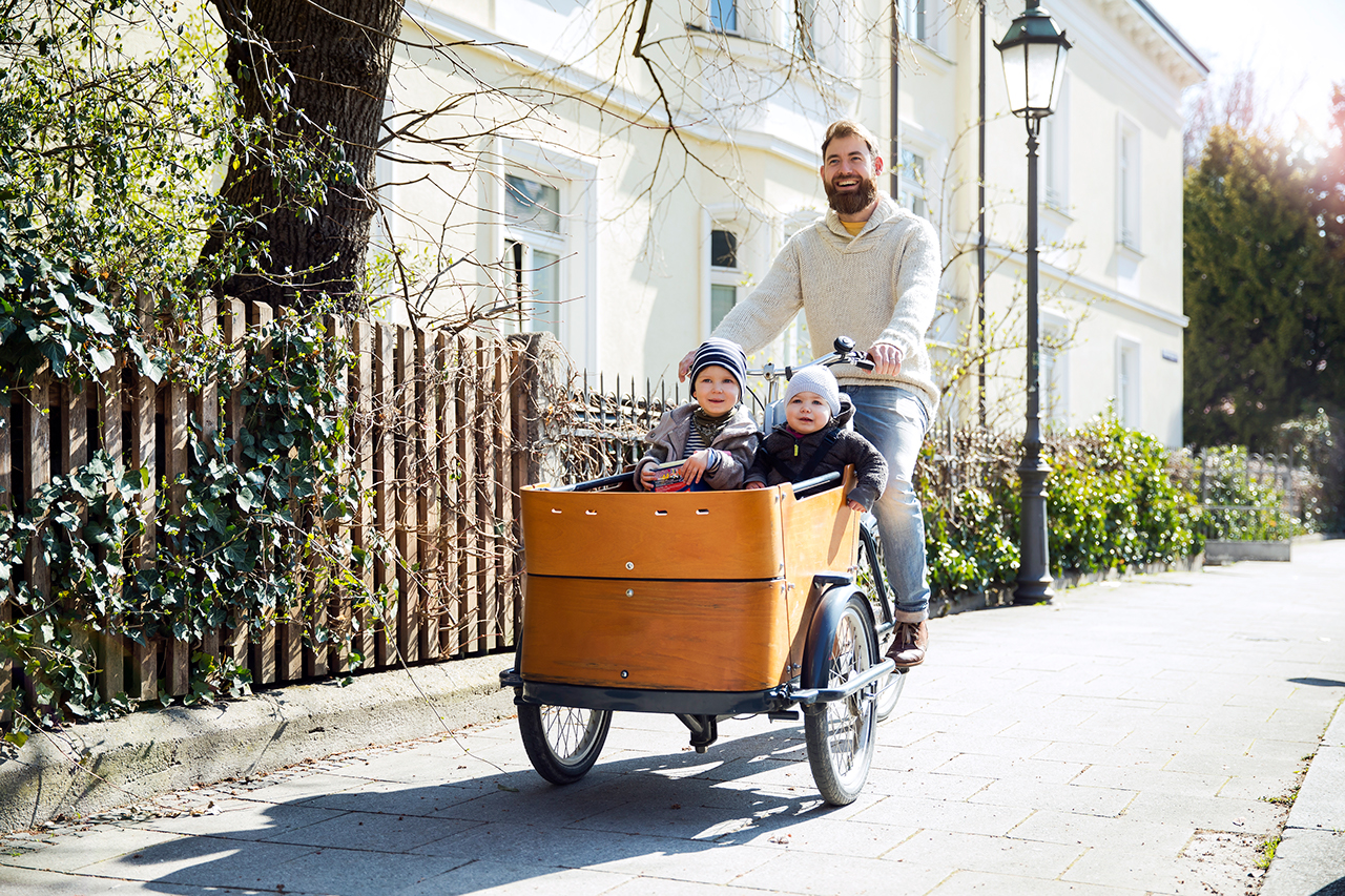 Happy father with two children riding cargo bike in the city.