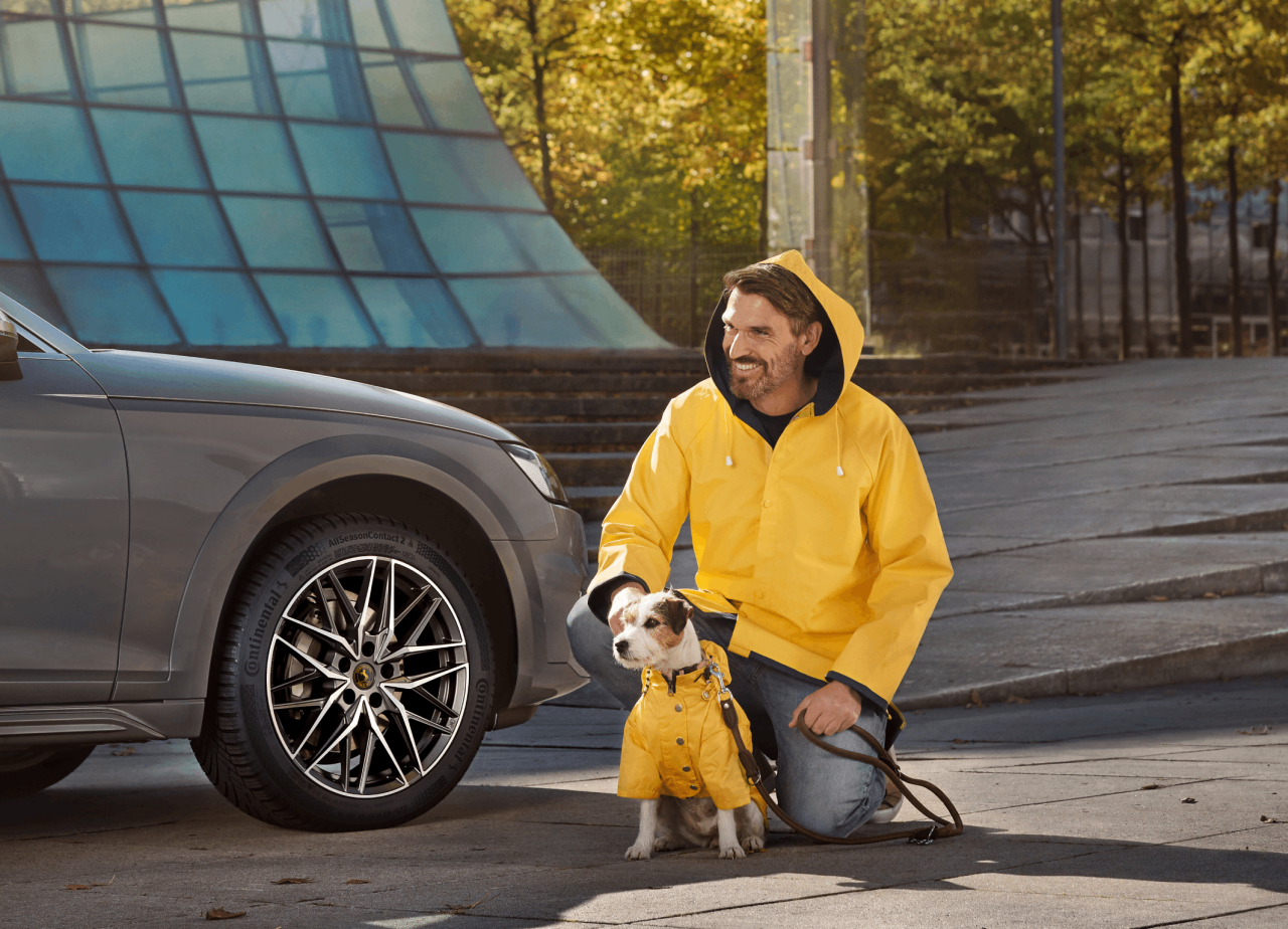 Véhicule équipé de pneus Continental AllSeasonContact 2, avec à côté un homme et un chien portant une protection contre la pluie.