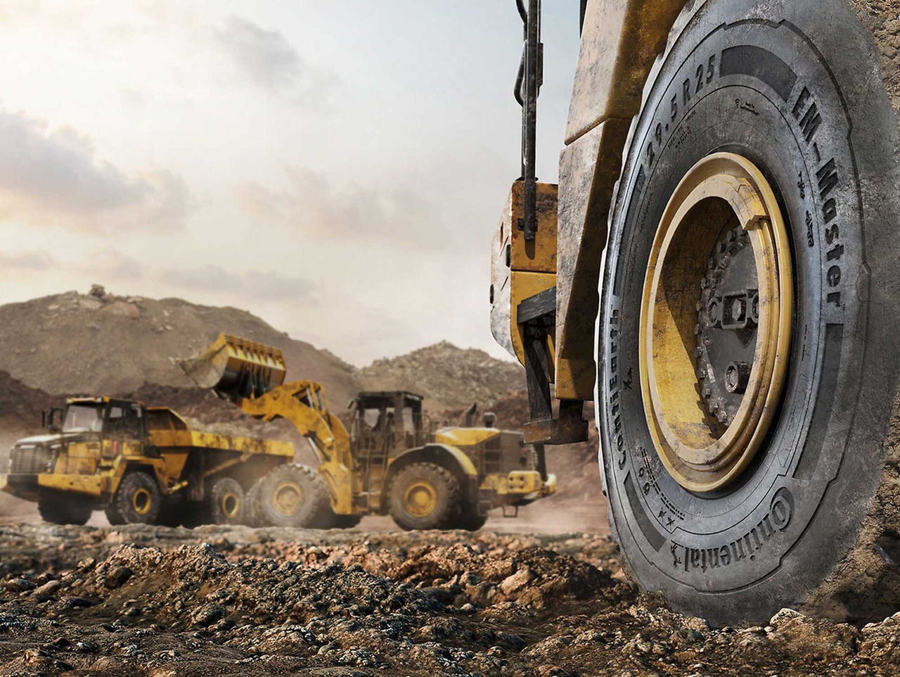 Llanta Continental OTR (La imagen muestra un escenario en una mina. En primer plano, vemos una llanta Continental OTR de una máquina grande, con características robustas, sugiriendo un ambiente de trabajo intenso y extremo. La llanta es negra con detalles amarillos, indicando la marca Continental. En el fondo se ven tres máquinas pesadas, como cargadoras y camiones, que trabajan en un terreno irregular y accidentado. El suelo es de tierra, con algunas piedras visibles, indicando que el lugar está siendo excavado o nivelado. El cielo de fondo está ligeramente nublado, con tonos claros de azul y gris, y la atmósfera sugiere un día de trabajo activo, con polvo en el aire debido al movimiento de las máquinas. La escena transmite una sensación de grandeza y actividad industrial.)