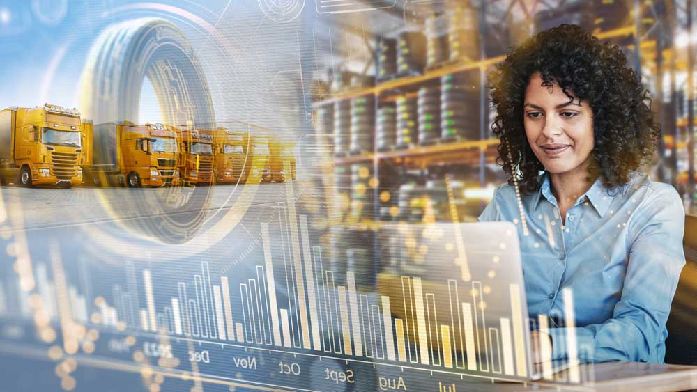 (Mujer trabajando en una laptop con gráficos de desempeño, mientras camiones amarillos se encuentran al fondo en un entorno logístico.)