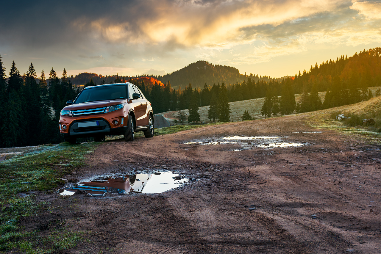 orange suv parked on the country road near forest in mountains at sunrise. beautiful autumn scenery. travel Europe by car concept