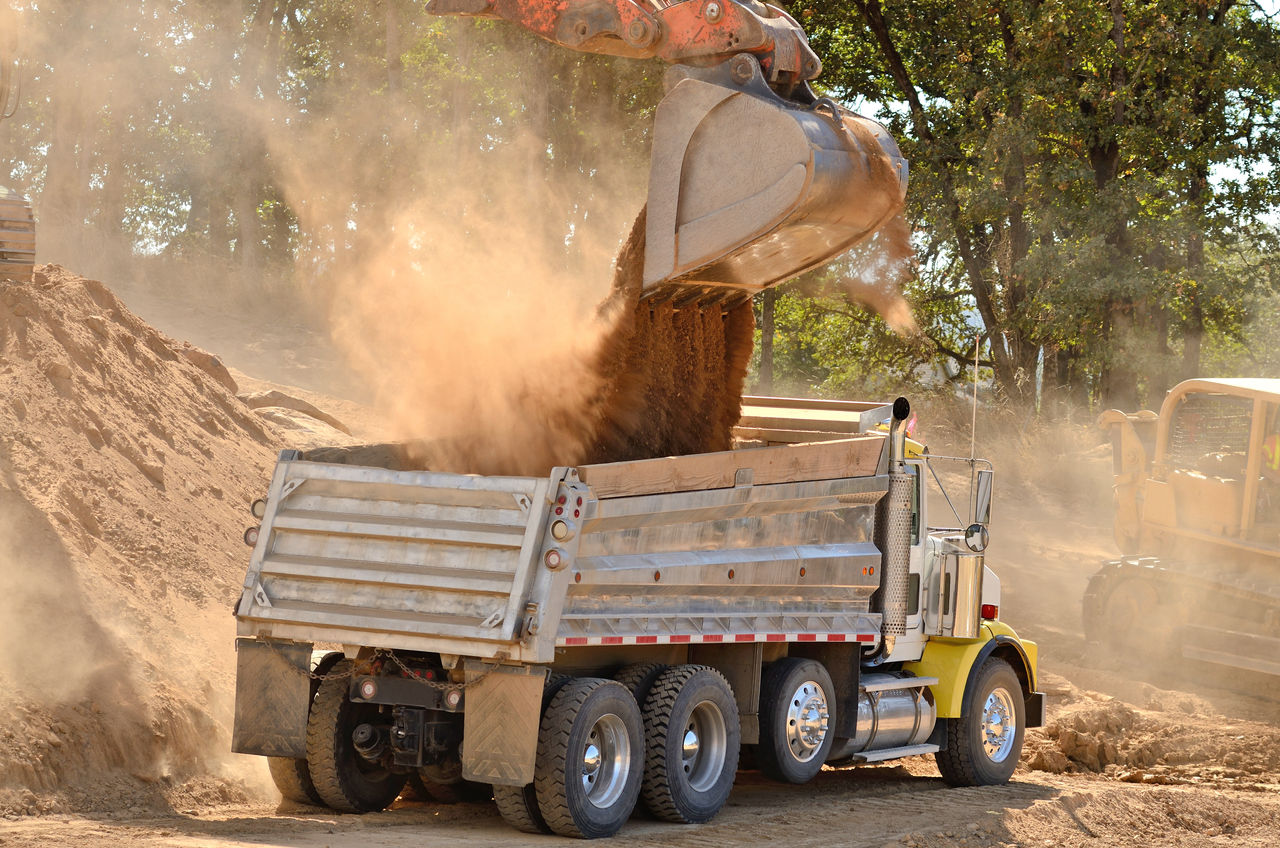 Large track hoe excavator filling a dump truck with rock and soil for fill for a new commercial development road construction project