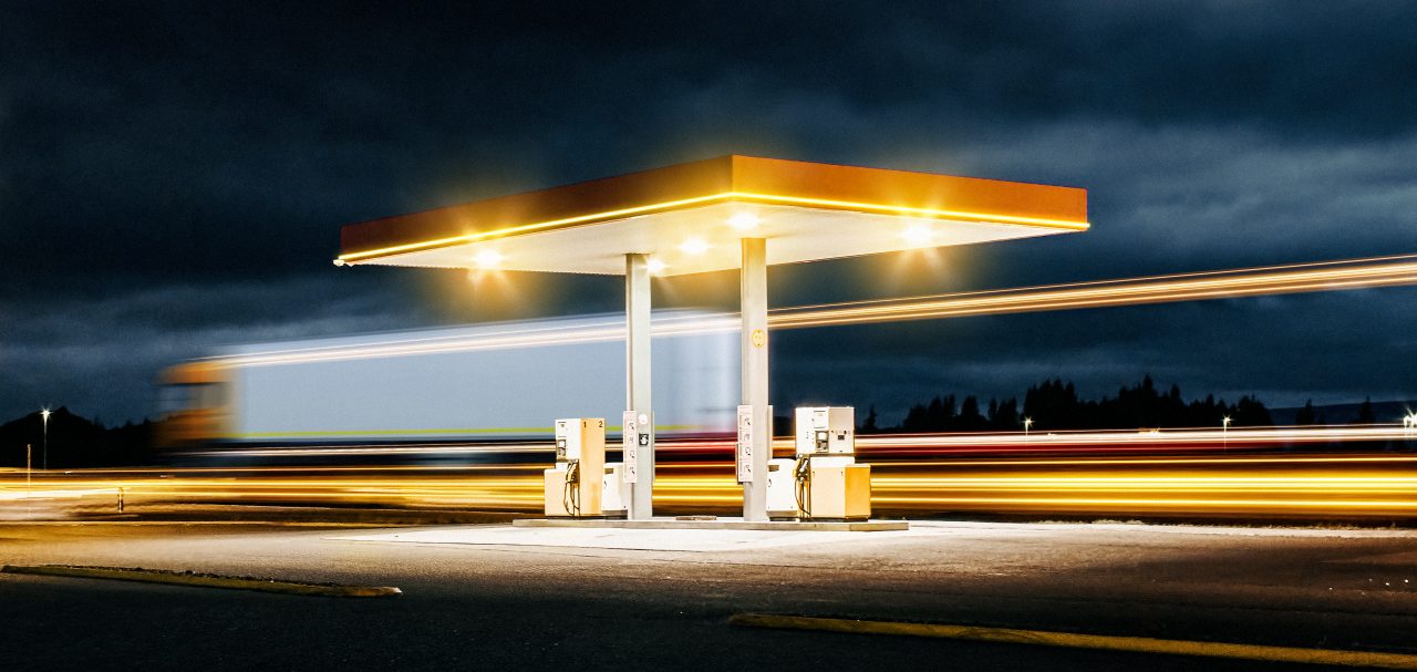 A Truck passes a gas station during night.