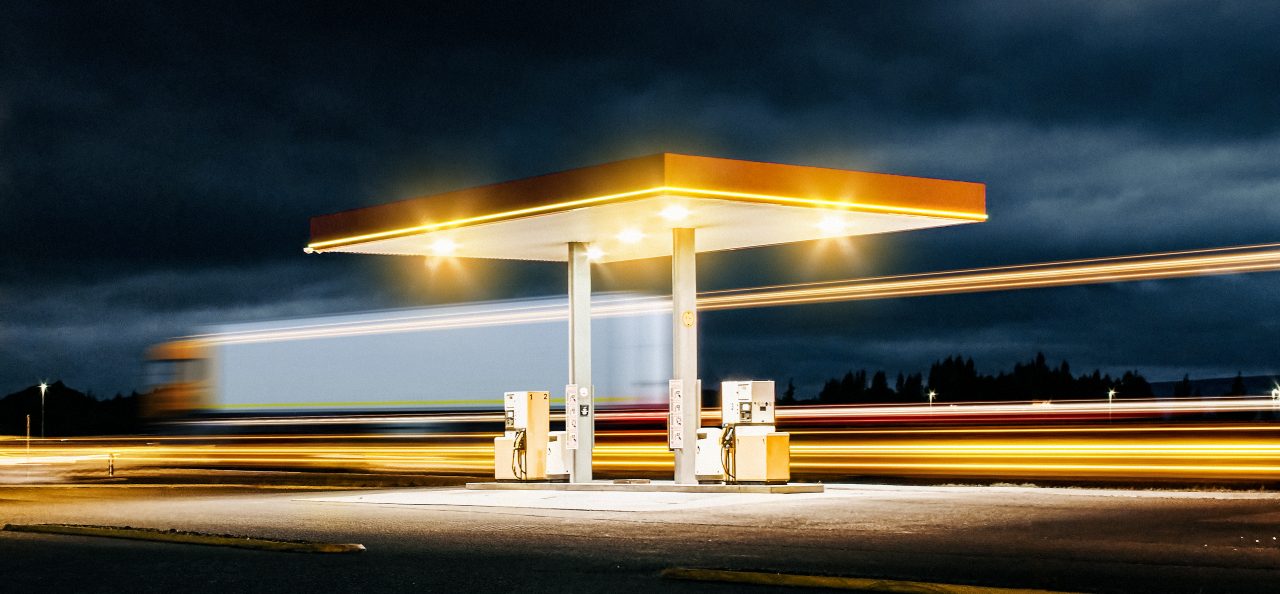 A Truck passes a gas station during night.