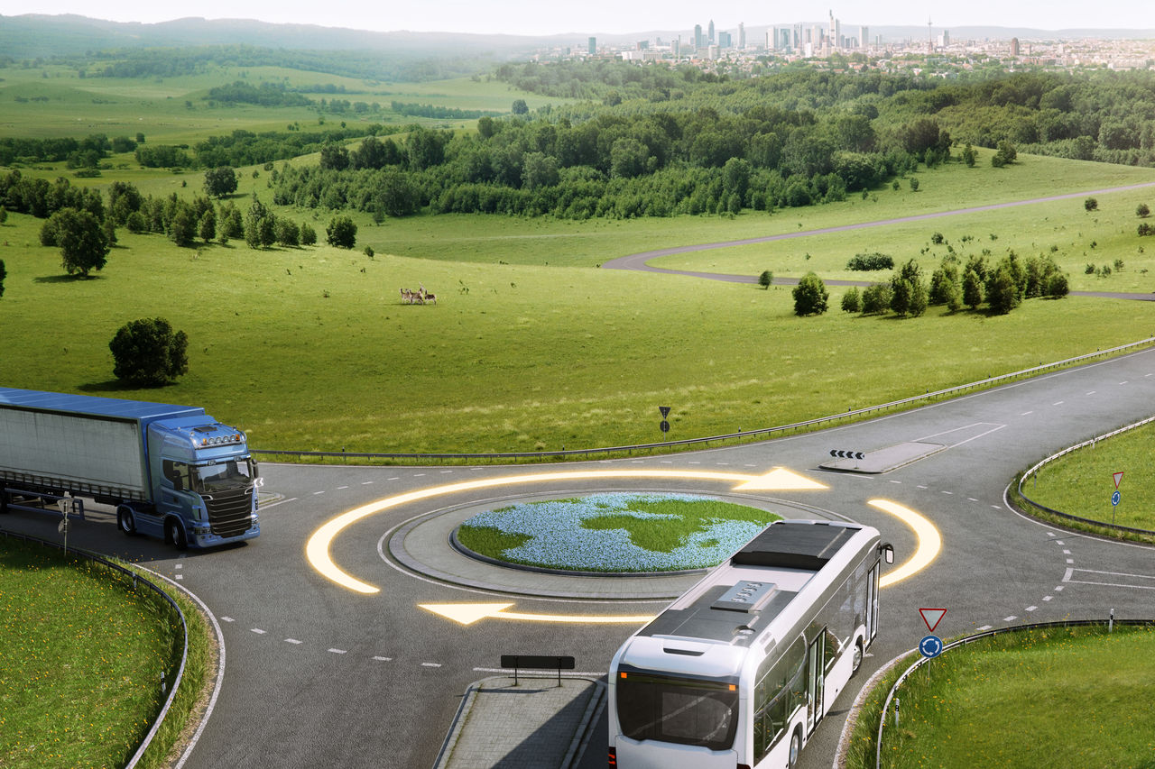 A bus and a truck approach a circular intersection with a grass design resembling Earth in the center.