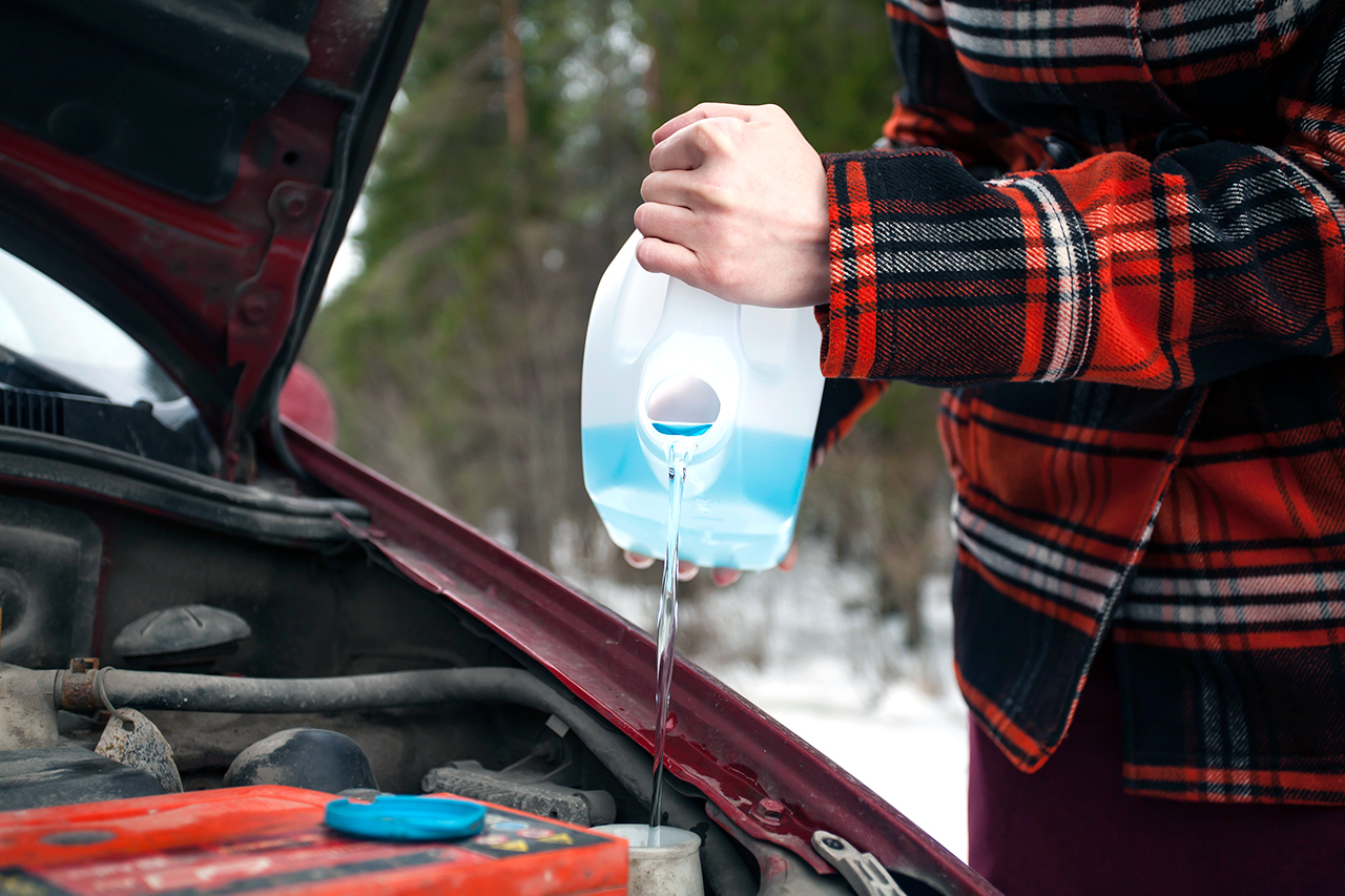 Closeup shot of hands holding bottle with antifreeze washer fluid and pouring it into windshield washer tank in winter day.