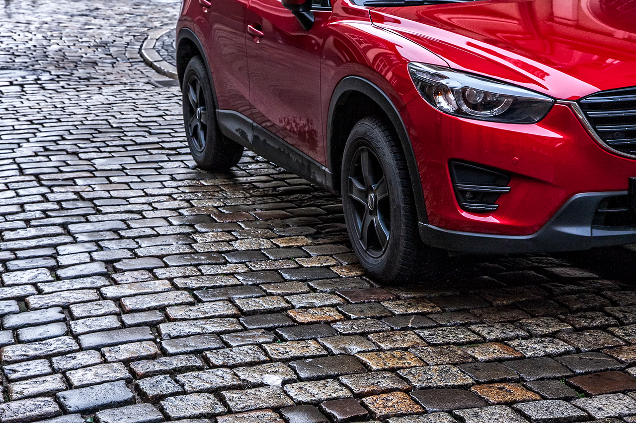 A red SUV is driving on cobble stones.