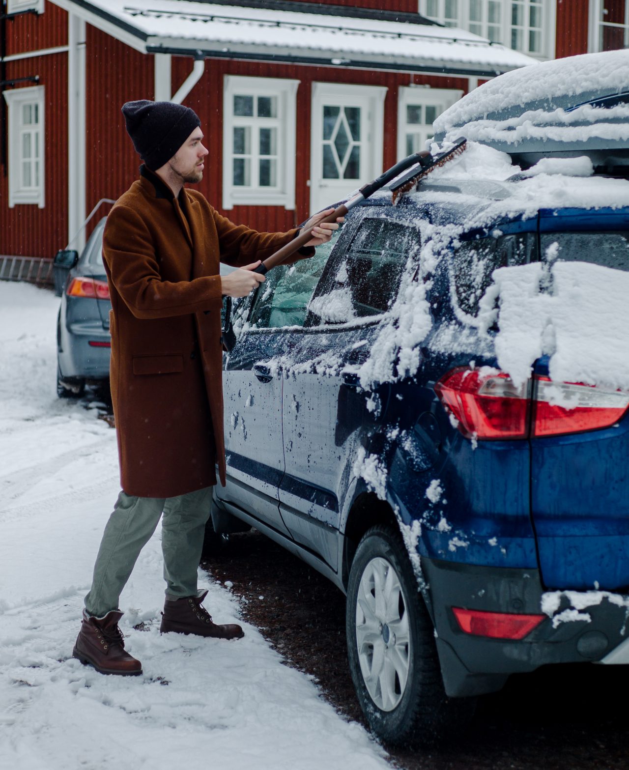 A man cleaning his car from snow in front of a house.