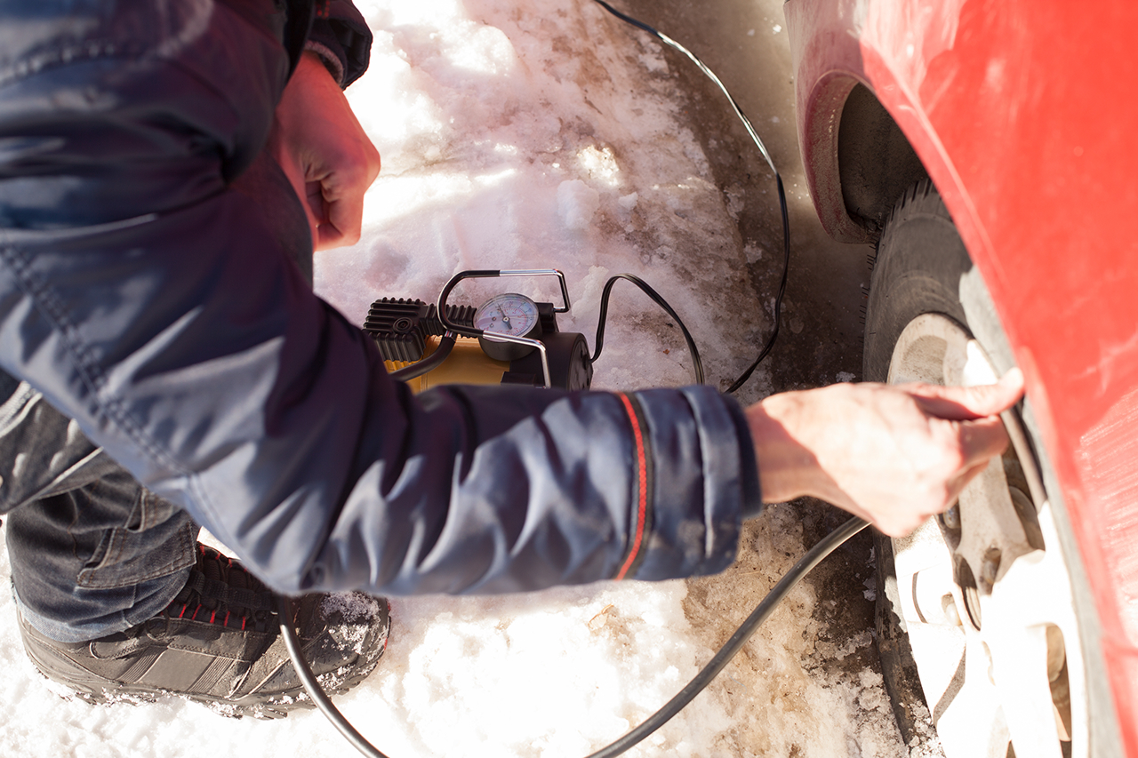 Inflating a tire on a red car in snow.