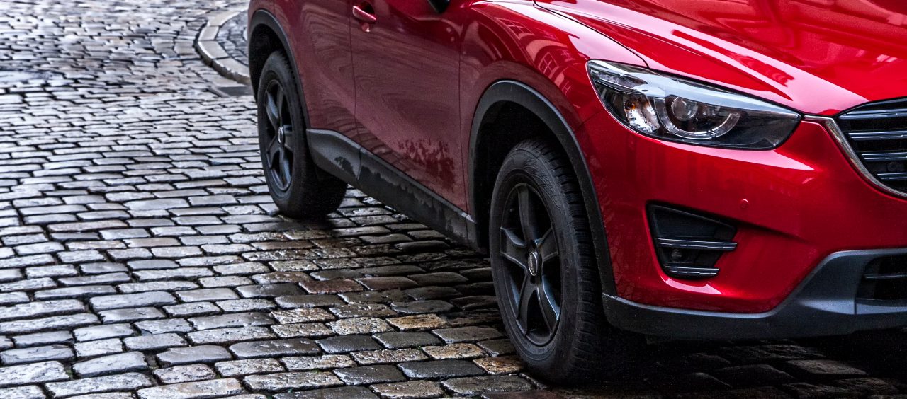 A red SUV is driving on cobble stones.