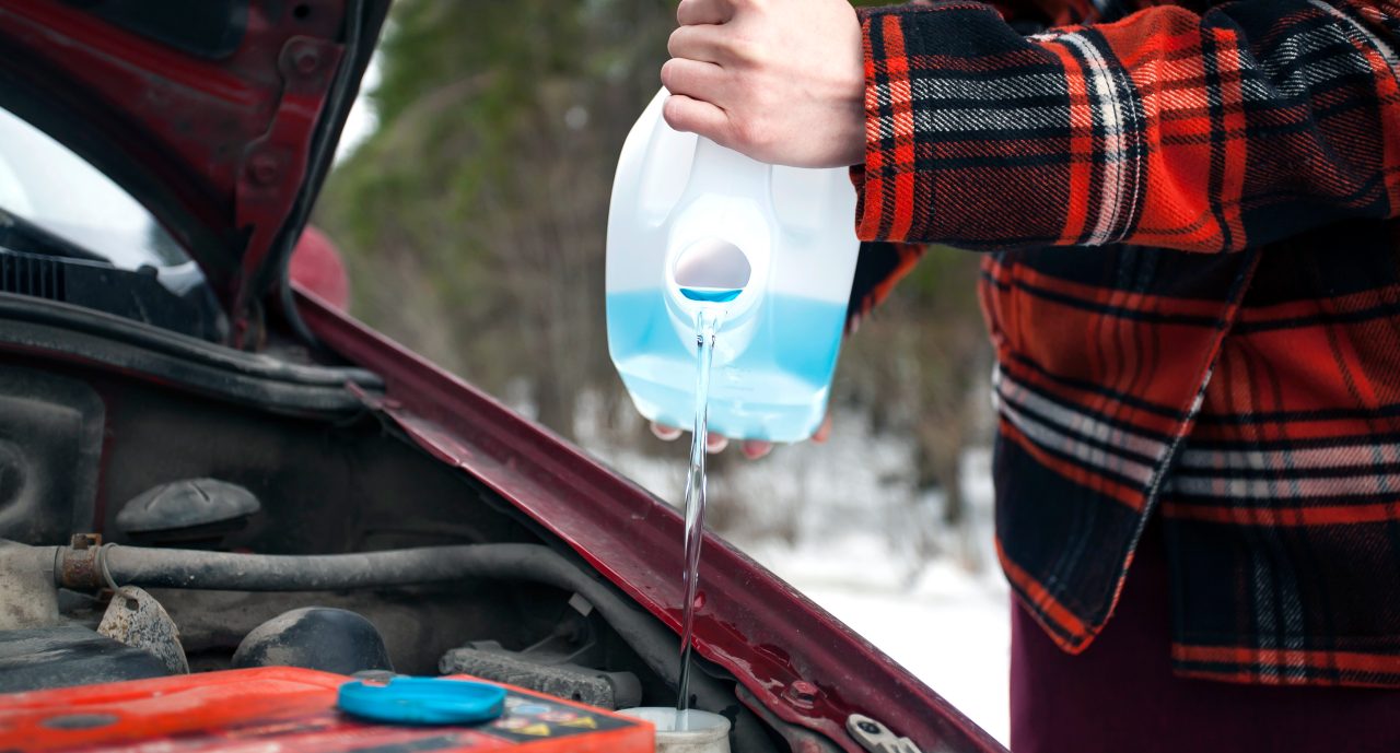 Closeup shot of hands holding bottle with antifreeze washer fluid and pouring it into windshield washer tank in winter day.