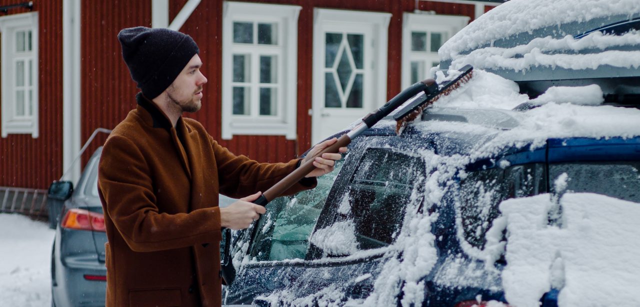 A man cleaning his car from snow in front of a house.