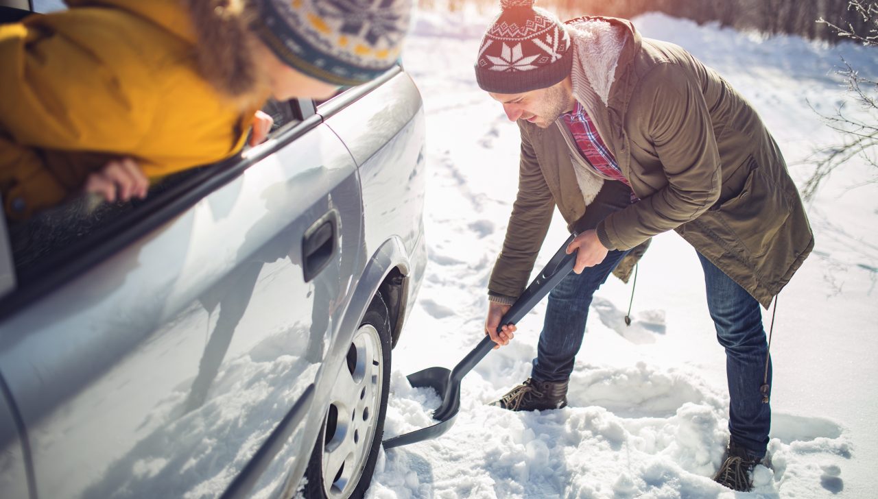 A man cleans snow near the car with shovel in nature.