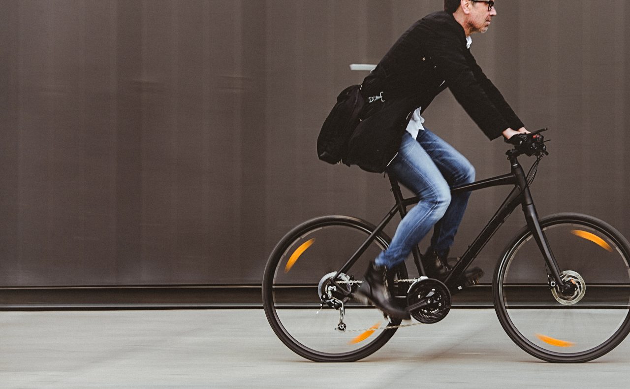 Handsome man, on the way to work, riding bicycle beside the grey wall. The man is casually dressed and wears eyeglasses and carries black briefcase hung on shoulder. Blurred motion, copy space has been left.