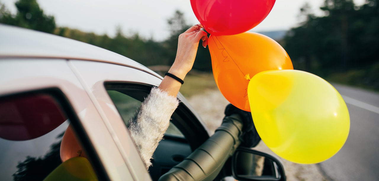 Young woman having fun while holding balloons through car window.
