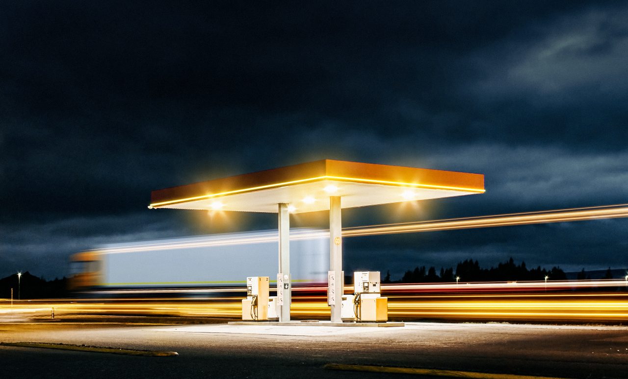A Truck passes a gas station during night.