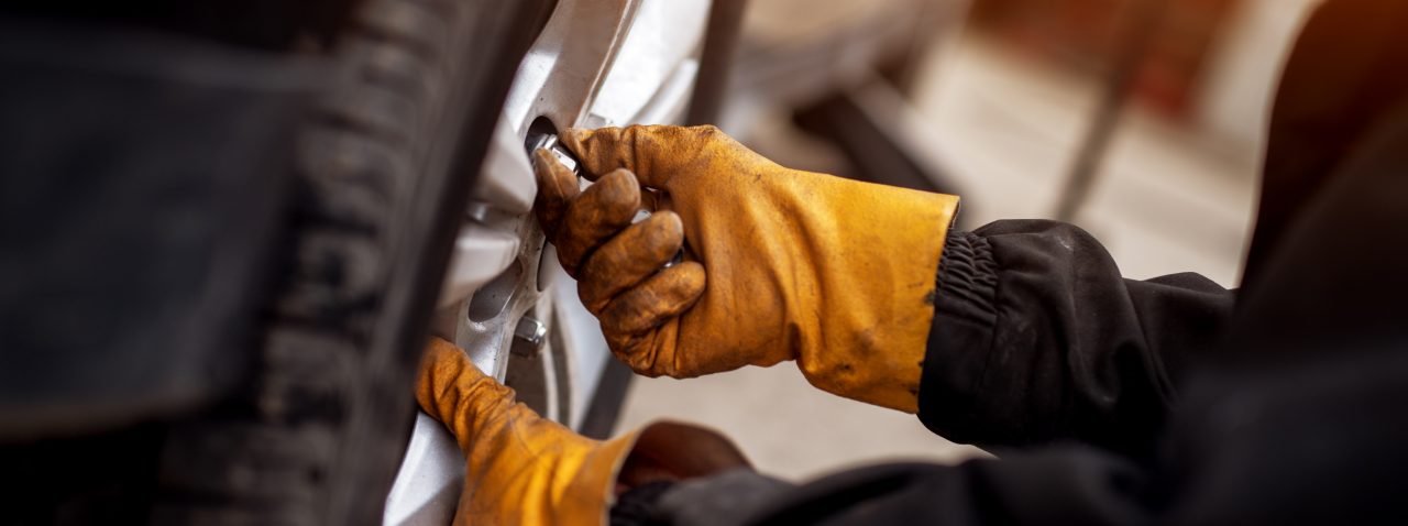En mekaniker med orange handskar sätter skruvar på ett placerat hjul på en bil.