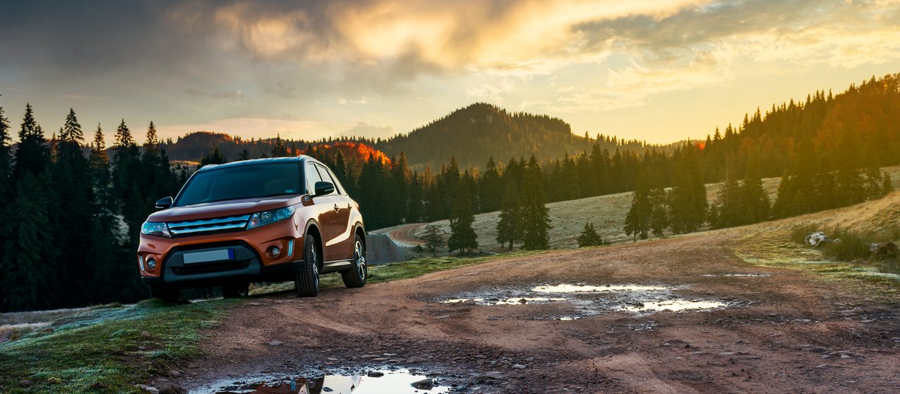 Orange suv parked on the country road near forest in mountains.