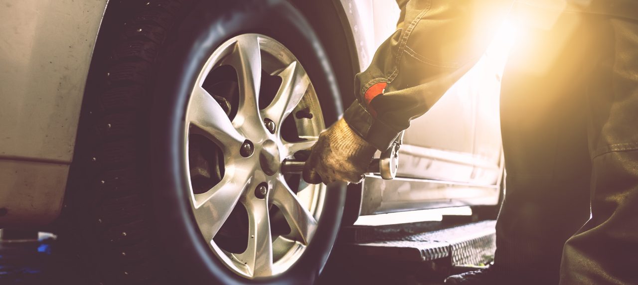 Mechanic hands with wrench changes wheel on car with special equipment in car repair service shop, sunlight effect, toned