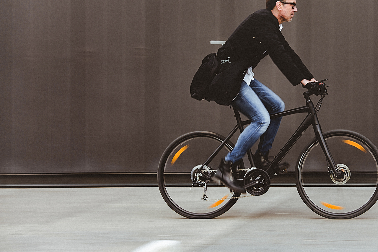 Handsome man, on the way to work, riding bicycle beside the grey wall. The man is casually dressed and wears eyeglasses and carries black briefcase hung on shoulder. Blurred motion, copy space has been left.
