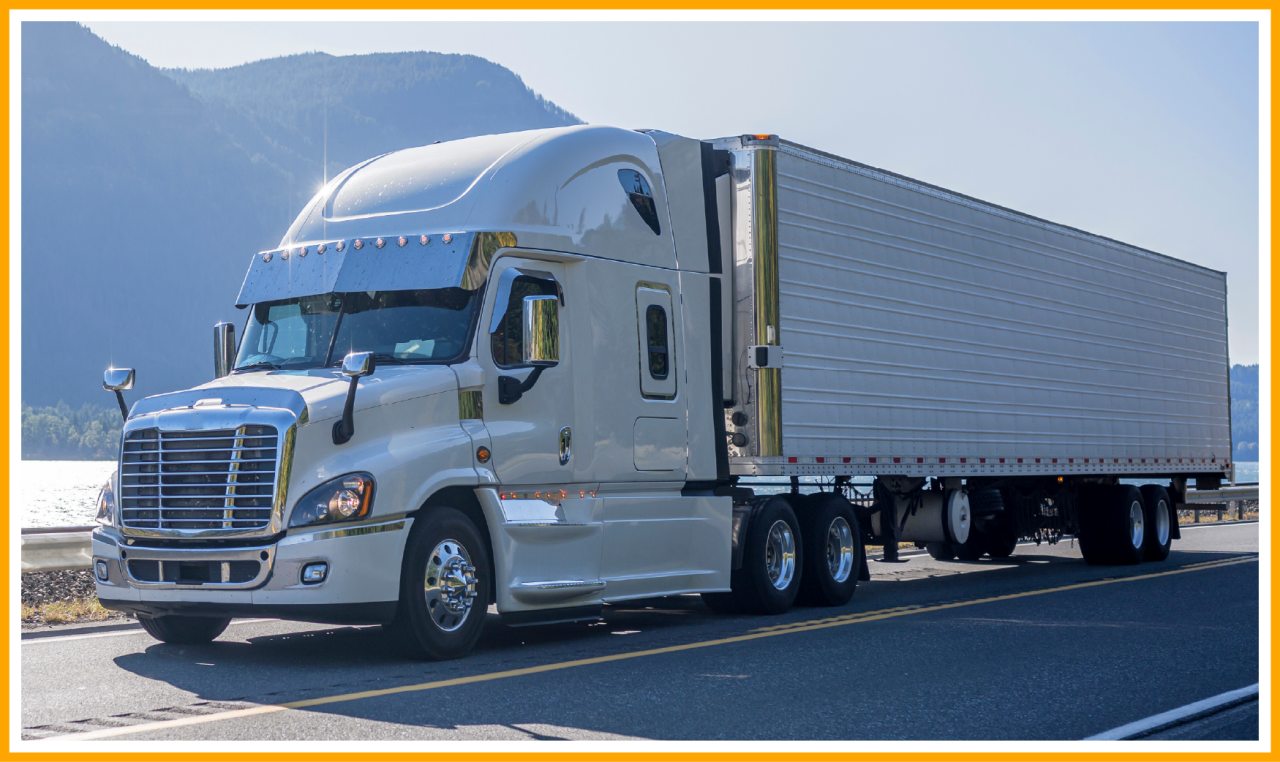 White semi-truck with trailer driving on a scenic road near mountains and a body of water.