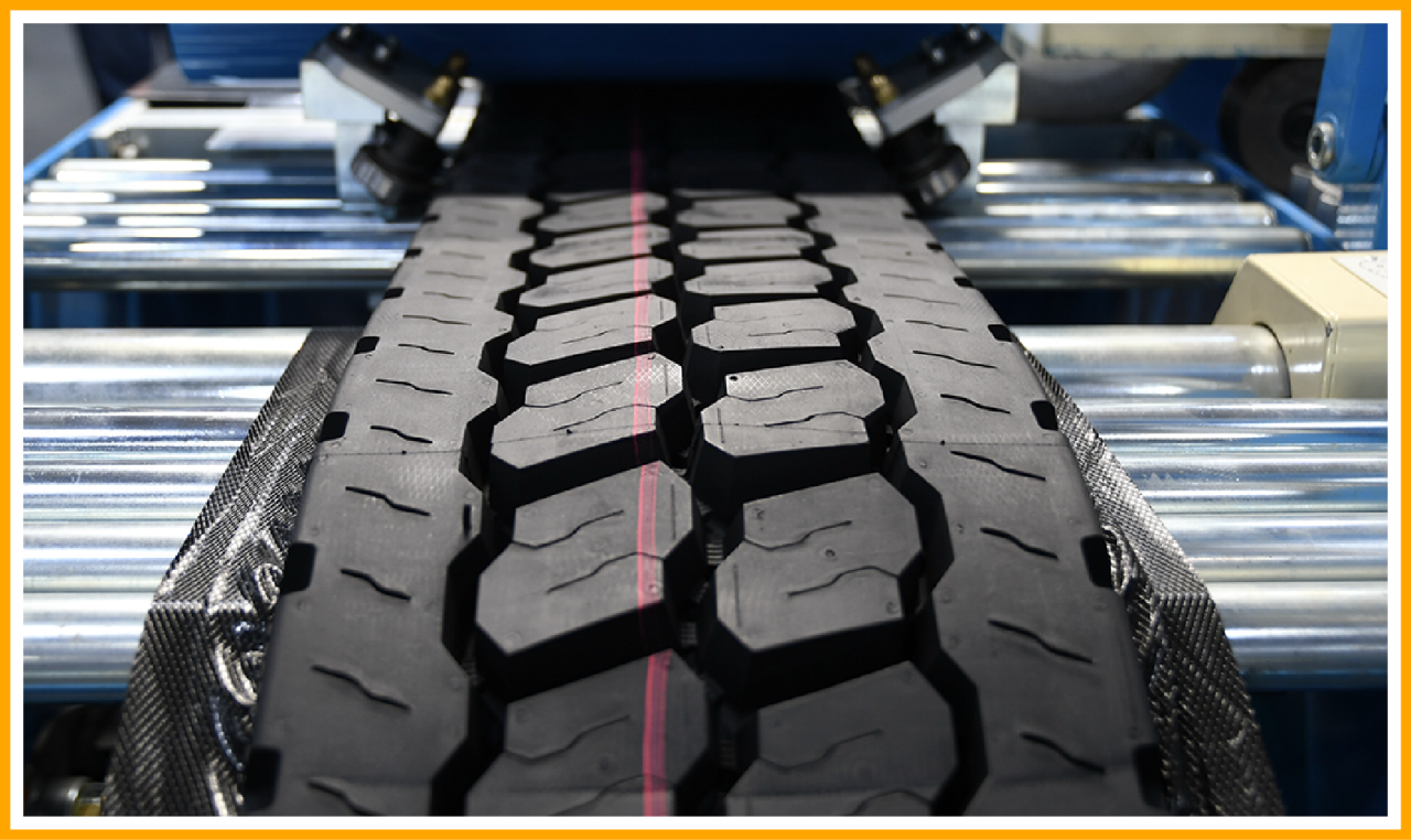 Close-up of a tire tread with hexagonal and rectangular patterns, featuring a red center line, on an industrial machine.