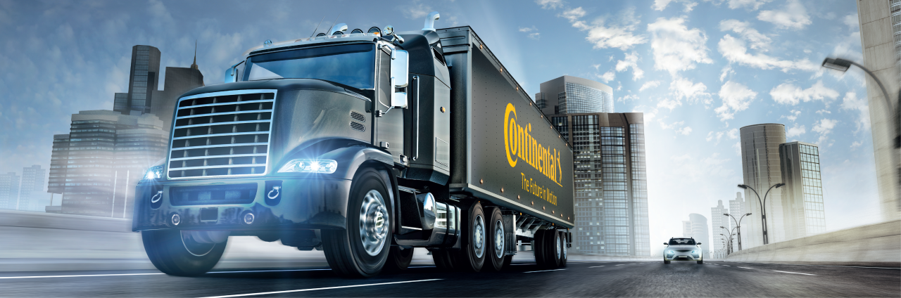 Black Continental semi-truck on urban highway with tall buildings and partly cloudy sky